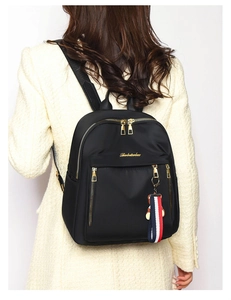 Women's black nylon backpack featuring a golden bear charm and tricolor strap detail
