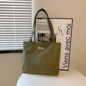 Close-up of green corduroy tote bag showing striped texture and Fashion patch detail