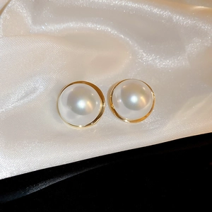 Close-up of French vintage round faux pearl earrings with gold trim on white silk fabric