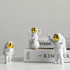 Three white astronaut figurines with gold visors set on books for modern desk decor