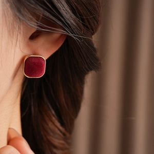 Close-up of red flocked velvet square earrings with gold metal frame on a model
