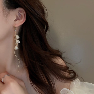 Détail de boucles d'oreilles muguet avec pompons floraux blancs et chaînes dorées