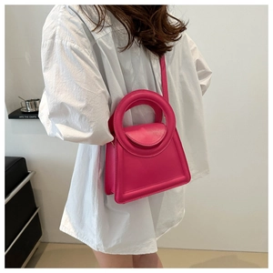 Close-up of rose red matte leather handbag with unique circular handle and slim strap