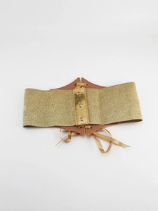 Detailed close-up of golden elastic waist belt with metal sheen and brown faux leather lace-up back