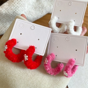 Close-up of velvet C-shaped hoop earrings with silver snowflakes in red, pink, and white