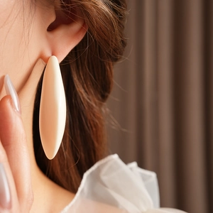 Gros plan d'une boucle d'oreille ovale en résine crème portée par un mannequin élégant