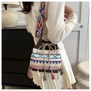 Detail of embroidered straw bucket bag with tassels and colorful geometric strap