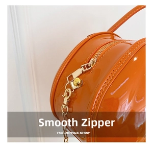 Detailed close-up of smooth gold metal zipper and glossy orange patent leather texture