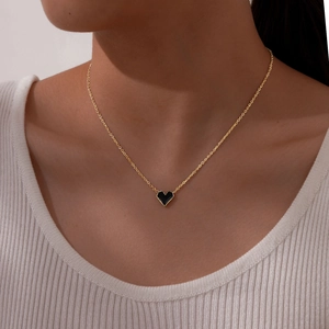 Detail showing a gold necklace with a black heart pendant worn by a model in lifestyle shot