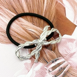 Detail showing a black elastic hair tie with a twisted silver metallic bow decoration