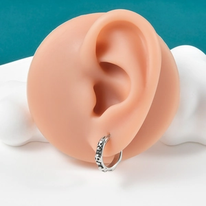 Close-up of vintage punk hoop earring with skull relief on a silicone ear model
