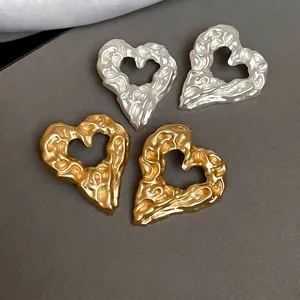 Irregular textured liquid metal heart earrings in gold and silver finish on grey background