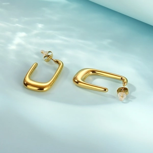 Detail of chunky gold U-shaped earrings with reflective finish over water ripples