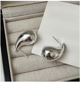 Macro detail of silver hollow teardrop earrings on a beige velvet jewelry box