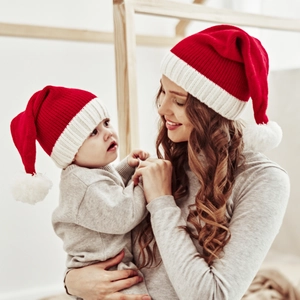 Matching red knitted Christmas hats worn by mother and baby in a warm festive setting