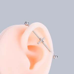 Close-up of silver industrial barbell with crystal cross pendant on an ear model