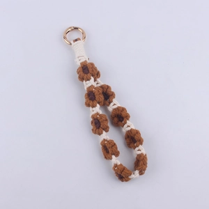 Close-up of handmade woven floral keychain with brown and white cotton cord and gold clasp