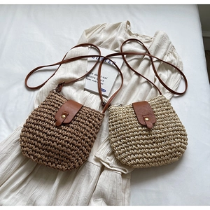 Detail view of mini woven straw bucket bags in brown and beige with leather strap