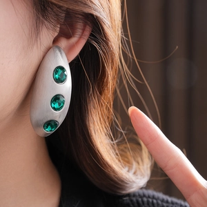 Macro view of brushed silver earring with three emerald green round gemstones on ear