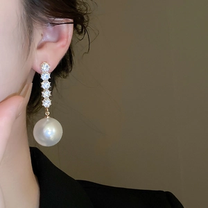 Close-up of elegant gold long drop earrings with shiny crystals and white pearls on a model