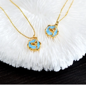 Macro shot of gold fish tail necklaces with blue enamel pendants on coral background