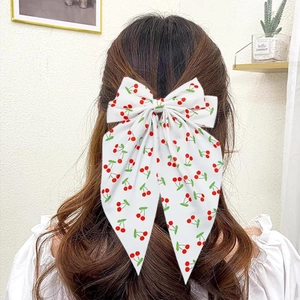 Sweet white bow hair clip with red cherry print worn by a woman on a half-up hairstyle
