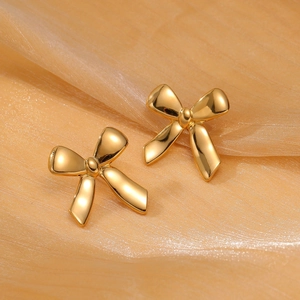 Detailed view of elegant gold bow stud earrings on luxurious champagne silk background