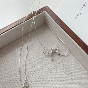 Macro detail of silver bow pendant on a sleek snake chain necklace with spring clasp