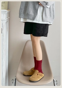 Detail of burgundy combed cotton socks worn with suede clogs in a cozy home setting
