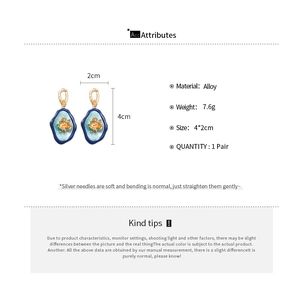 Vue détaillée des boucles d'oreilles ovales en émail bleu avec fleurs dorées et tailles
