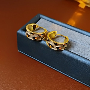 Detailed macro shot of vintage gold-plated C-shaped earrings with leopard enamel in a box