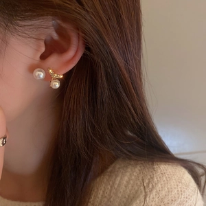 Close-up of elegant gold fishtail earrings with sparkling rhinestones and white pearls