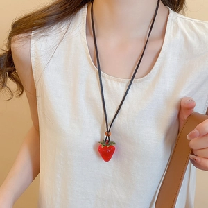 Detailed close-up of a red strawberry pendant necklace worn by a woman with a minimalist cord