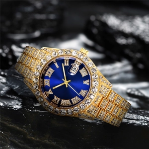 Macro shot of gold-tone iced out watch with blue dial and date window on black stone