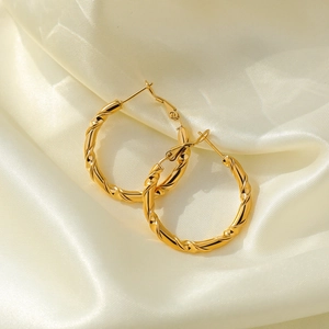 Detail of twisted gold hoop earrings placed on elegant white silk background