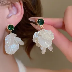 Elegant emerald green gemstone earrings with white pearl petals and gold trim on a model