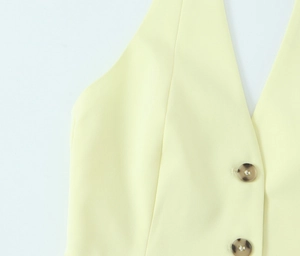 Detail of light yellow vest featuring V-neckline and dark amber-textured buttons