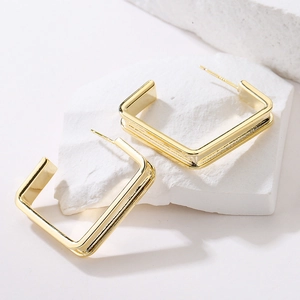 Minimalist gold plated square C-shape earrings on a white marble stone textured background
