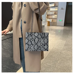 Detail shot of stylish snakeskin pattern chain bag worn with a chic beige coat