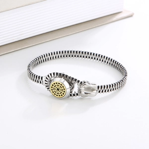 Detail shot of silver zipper bracelet with gold sunburst motif on a white background