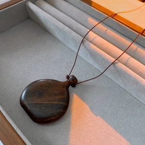 Detailed view of a vintage dark wood gourd pendant necklace inside a jewelry gift box