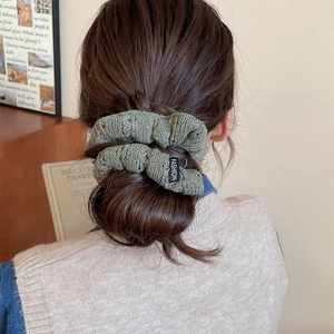 Dark green knitted scrunchie with fashion label worn on a ponytail in a cozy setting