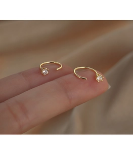 Macro shot of gold J-shaped earrings with six-prong set cubic zirconia on a finger