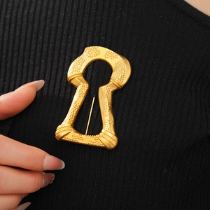 Detail of vintage gold keyhole brooch with embossed texture on black knitwear