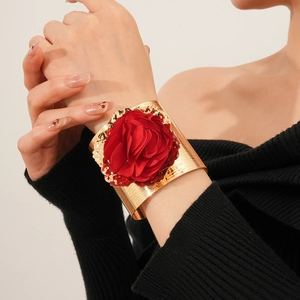 Gros plan d'un large bracelet manchette doré orné d'une fleur détaillée en tissu rouge