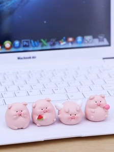 Close-up of four mini pink resin pig ornaments on a laptop keyboard desk decor