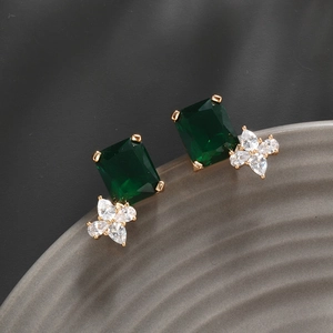 Macro shot of emerald green drop earrings with flower zircon accents on a gray ceramic plate