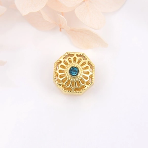 Detailed view of an 18k gold-plated hexagonal charm with a central blue round gemstone