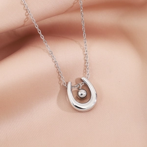 Silver horseshoe pendant necklace with polished bead on a pink satin fabric