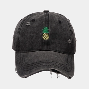 Close-up of pineapple embroidery and distressed ripped details on a washed black cotton cap